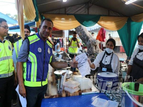 Mohd Noor (kiri) menyerahkan risalah kepada para peniaga bazaar Ramadan Taman Kerang, semalam.