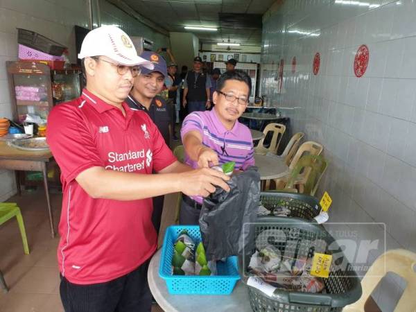 Syeikh Azhari (kiri) memeriksa bungkusan nasi dijual di kedai makan Cina di Pekan Tunjang, di sini, hari ini.
