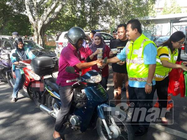 Azman (kanan) turut mengagihkan bubur lambuk kepada pengguna jalan raya di hadapan SMK Agama Kedah, petang tadi.