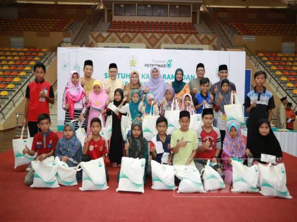 Wan Mohd Hasnan Abdullah (belakang dua dari kanan) dan Tengku Hassan (belakang dua dari kiri) bersama sebahagian murid yang dirai dalam majlis berbuka puasa sempena program Sentuhan Kasih Yayasan Petronas 2019 di Stadium Negeri.