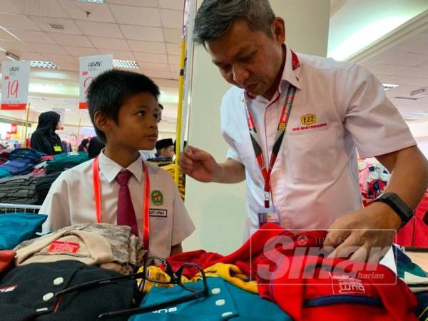 Jamal (kanan) mencuba pakaian baharu kepada salah seorang penerima bantuan program berkenaan di Plaza Angsana, Johor Bahru, hari ini.