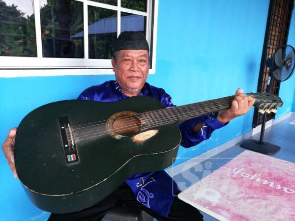 Cikgu Sudin menunjukkan gitar buruk yang menjadi peneman dia mengajar. 