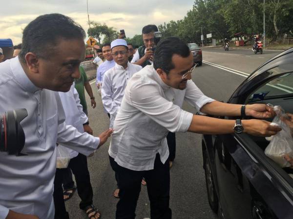 Dr Asyraf (kanan) dan Rezaal (kiri) mengedar bubur lambuk kepada orang ramai di Taman Bertam Indah, petang tadi.