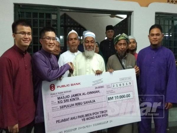 Kah Woh (dua dari kiri) menyerahkan replika cek kepada Shahril di perkarangan Masjid Al-Dinniah, Kampung Sri Kinta di sini malam tadi.