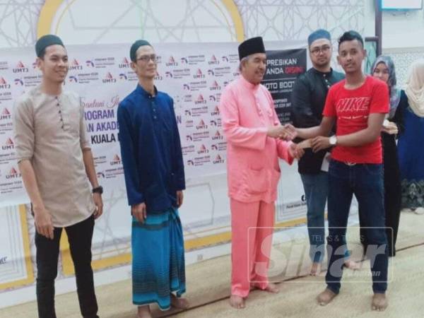 Md Adam (kiri) menyampaikan baucar kepada pelajar pada majlis berbuka puasa di Pusat Islam Sultan Mahmud, UMT, semalam.