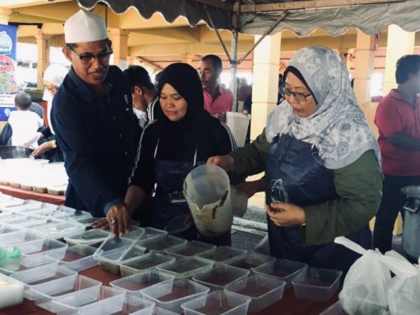 Fuziah (kanan) memasukan bubur lambuk ke dalam bekas untuk diagihkan kepada orang ramai selepas pada Program Memasak Bubur Lambuk Q-Fish dan Promosi Jualan Ikan di Pasar Nelayan Sepat hari ini.