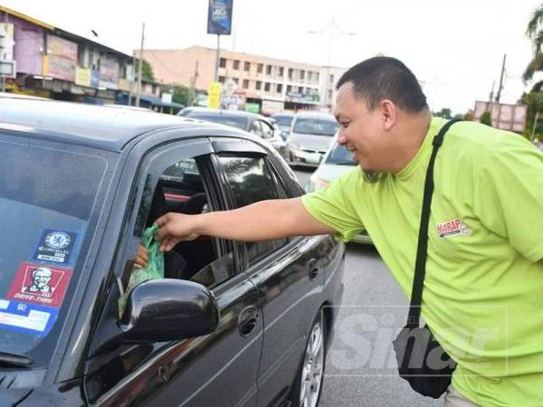 Ahmad Nazmi mengagihkan ABC kepada pengguna jalan raya di lampu isyarat Pulau Kambing, Kuala Terengganu, semalam.