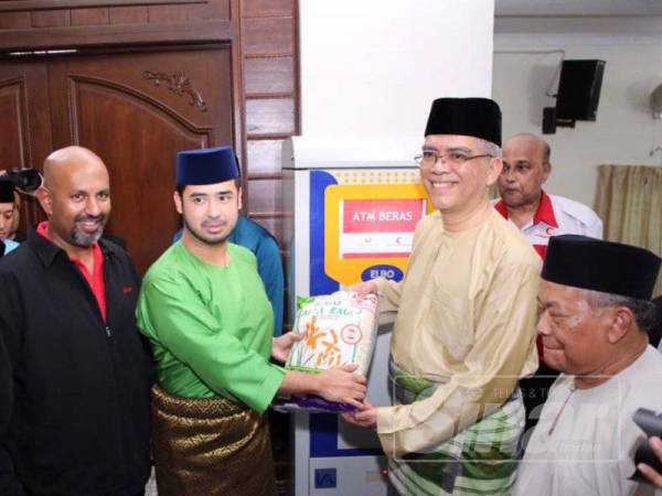 Tunku Idris (dua,kiri) menerima satu bungkusan beras dari Khairil untuk diisi ke dalam mesin ATM berkenaan sebagai gimik pelancaran majlis di Masjid India hari ini.