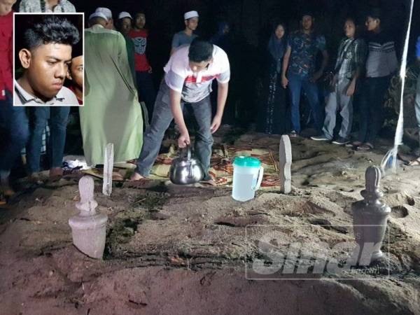 Muhammad Adib menyiram air di pusara kedua-dua ibu bapanya yang selamat disemadikan dalam satu liang lahad di Tanah Perkuburan Islam Kampung Dura Tengah, Dungun.