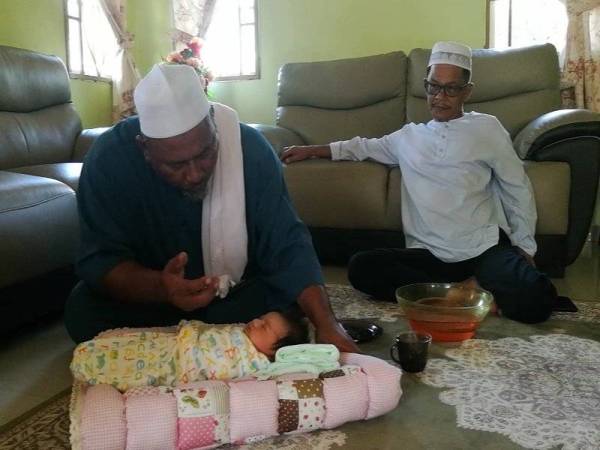 Allahyarham Ustaz Din ketika melakukan tahnik seorang bayi sambil diperhatikan Sanusi di sebuah rumah penduduk baru-baru ini.