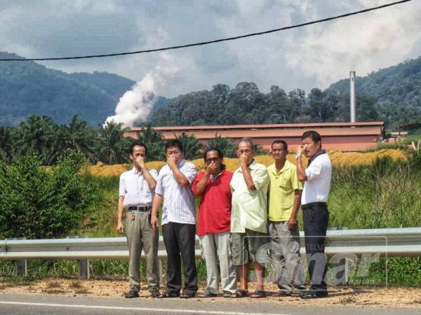 Chen Choo (dua, kiri) ketika mengadakan lawatan kerja, kelmarin bersama sebahagian penduduk yang menunjukkan kilang sawit di belakang mereka yang menghadapi pencemaran bau. 