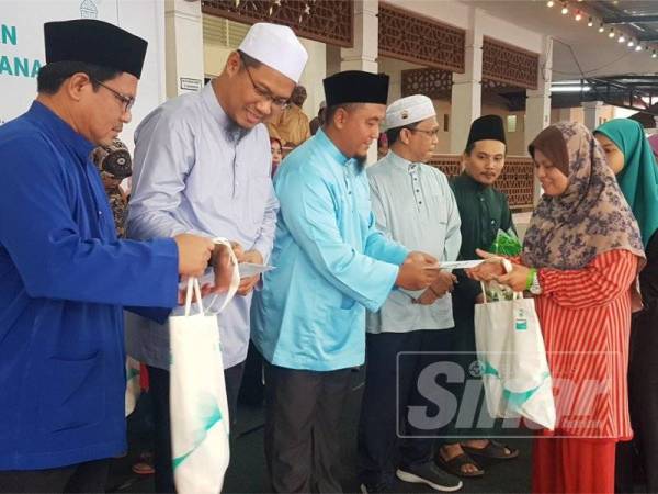 Wan Mohd Hasnan (kiri) dan Mohd Jukris (dua dari kiri) membantu Saiful Azmi menyampaikan sumbangan kepada penerima pada Program Sentuhan Kasih Ramadan Yayasan Petronas di Masjid Tebing Tembah, Paka, semalam.