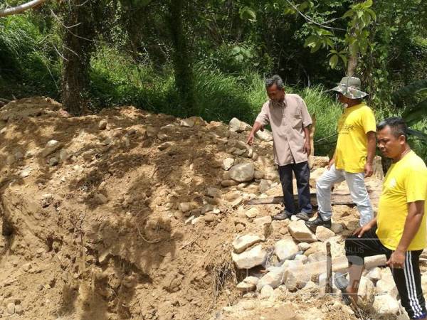 Sidik (kiri) bersama Saidi (kanan) dan seorang penduduk kampung melihat kawasan parit yang sebelum ini tersumbat akibat banjir lumpur.