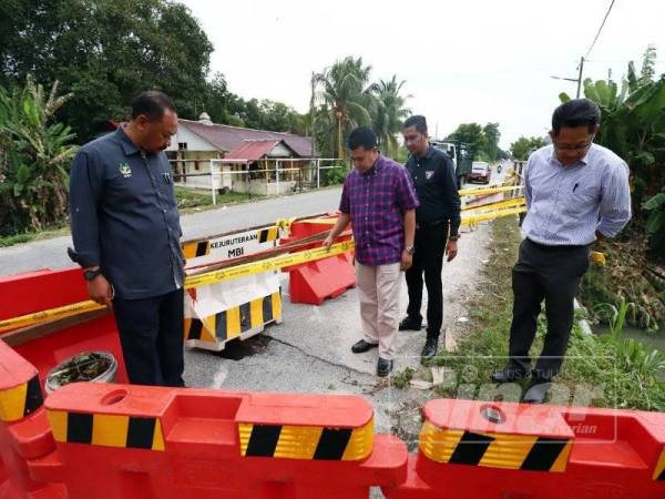 Ahmad Khair Faizal (dua, kiri) dan Khairul Anuar (kiri) meninjau keadaan Jambatan Kampung Tawas yang berlubang dan ditutup kepada orang ramai.