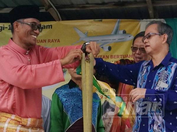 Boon Chye (kanan) membelah lemang sebagai gimik perasmian program Karnival Syawal @ Sekolah Agama Rakyat At-Tolibiah di Kampung Changkat Larang, Lahat hari ini.