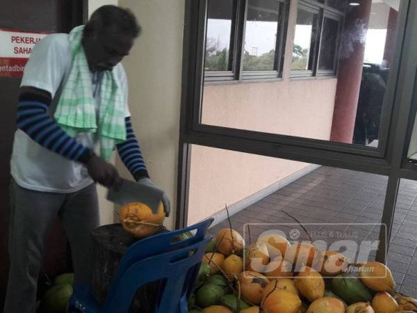 George membelah buah kelapa muda untuk diedarkan kepada petugas.