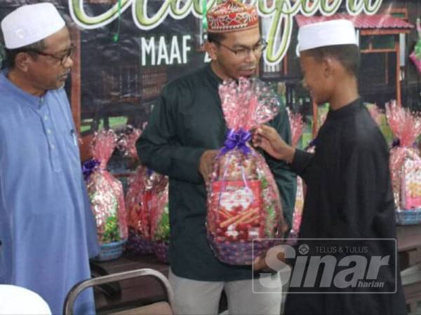 Mohd Fazil (tengah) menyampaikan hamper kepada anak penduduk di Surau An Nur, semalam.