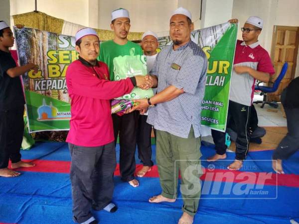 Muhammad Hishamudin (kiri) menyampaikan sumbangan kepada wakil penduduk dalam program tersebut.