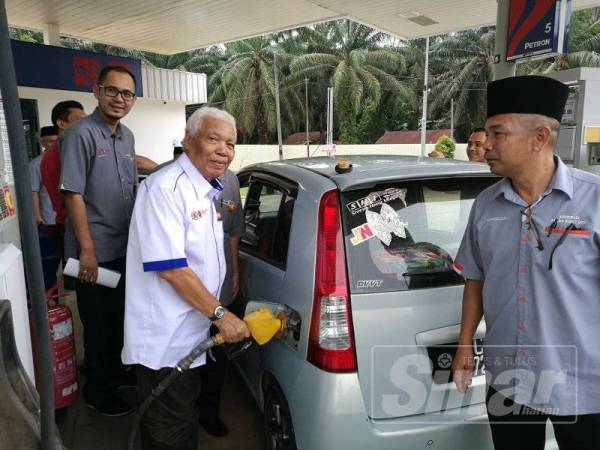 Nordin mengambil peluang mendekati masyarakat setempat dengan membantu mengisi minyak kenderaan pelanggan selepas menyempurnakan perasmian stesen minyak milik Koperasi Serbaguna Felda Bukit Goh Berhad sambil disaksikan Mohamad Zaidi (kanan).