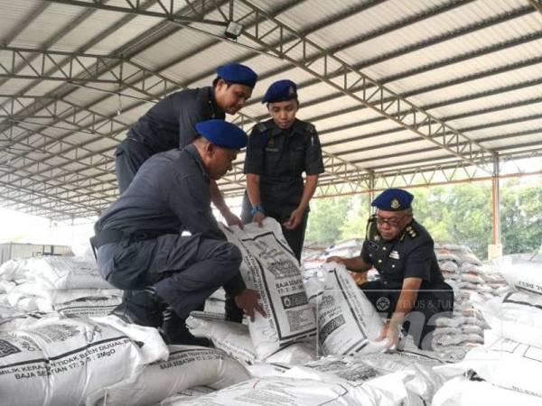 Omar (kanan) menunjukkan sebahagian baja kawalan tanpa lesen dirampas KPDNHEP di Sanglang dan Kampung Kuala Kerpan, Ayer Hitam kelmarin.