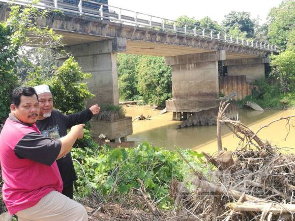 Mansor (kanan) bersama penduduk menunjukkan cerucuk jambatan yang kelihatan akibat hakisan pasir.