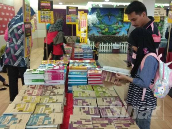 Azimuhaiza (dua dari kanan) bersama anaknya, Alisha Azzahira, 8 sedang memilih buku latihan yang dijual pada Jualan Gudang Pertengahan Tahun Karangkraf di Seksyen 15 di sini.