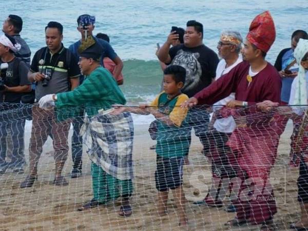 Ariffin (kiri) memeriahkan acara menarik pukat selepas merasmikan program diadakan di pantai peranginan Kelulut.