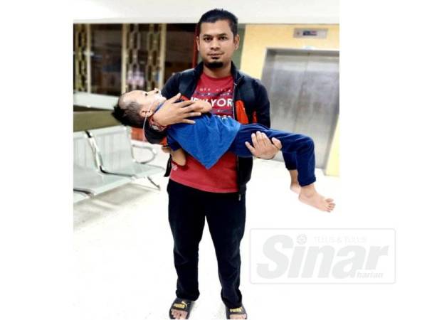 Mohd Bukhari memangku Muhammad Fawwaz Adli yang kini hanya terlantar selepas dibenarkan pulang dari hospital.