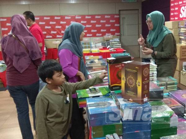 Seorang kakitangan (kanan) memberi penerangan mengenai produk naskhah al-Quran kepada pengunjung.