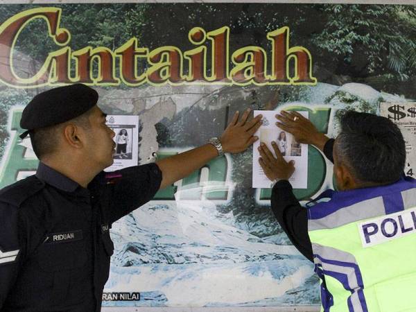 Dua anggota polis menampal kenyaataan dan gambar remaja Ireland, Nora Anne Quoirin, 15, pada papan tanda hentian bas hari ini sebagai alternatif mencari mangsa yang hilang Ahad lepas di sebuah resort di Kampung Pantai. - Foto BERNAMA