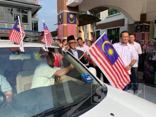 Samsudin (kanan) mengiringi Wan Rahim (tengah) menyampaikan bendera Jalur Gemilang kepada wakil-wakil yang menyertai konvoi tersebut hari ini.