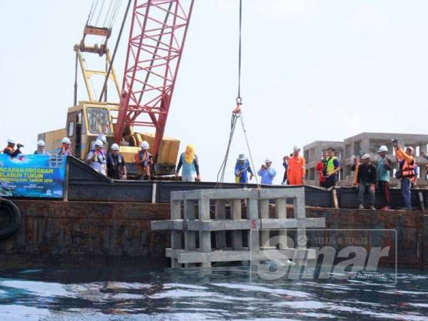 Azman (tengah) menyaksikan kerja menurunkan tukun dasar lembut di perairan Setiu hari ini.