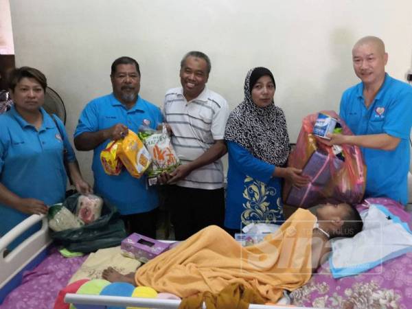 Pui (kanan) menyerahkan keperluan harian Faiz kepada ibunya, Sarimah (dua, kanan) ketika lawatan mereka ke rumah murid itu di Taman Tiong hari ini.
