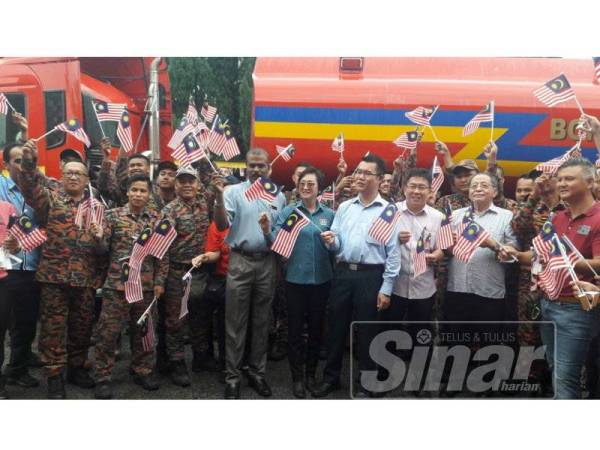 Chen Choon (depan, empat dari kanan) bersama Kit Siang (tiga dari kanan) mengibarkan Jalur Gemilang bersama anggota bomba yang terlibat dalam operasi kebakaran di Kampung Pekajang.