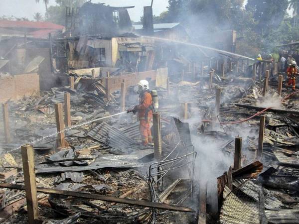 Anggota Jabatan Bomba dan Penyelamat sibuk memadamkan kebakaran membabitkan empat rumah di Kampung Padang Pohon Tanjong hari ini. - Foto BERNAMA