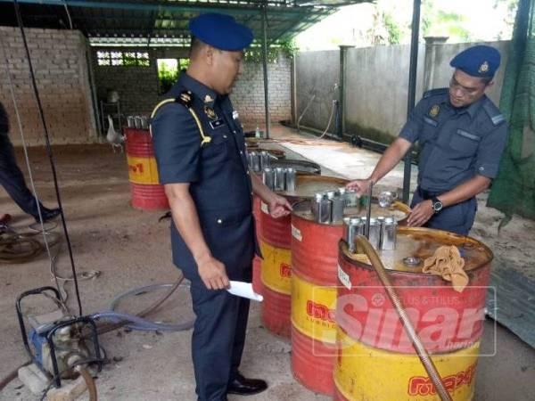 Mohamad Amri (kiri) memeriksa tong drum berisi minyak petrol dalam serbuan di Kampung Melayu di sini hari ini.