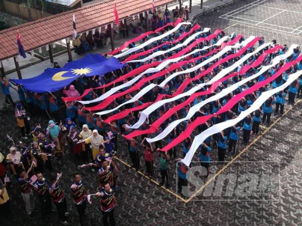 Murid SK Alor Keladi mengibarkan kain yang dicantumkan menjadi jalur gemilang disertai guru mereka di sekolah itu hari ini.