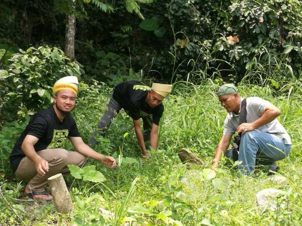 Zaid kiri menunjukkan salah satu makam dalam kawasan semak dengan bahagian atas batu nisan itu telah patah.