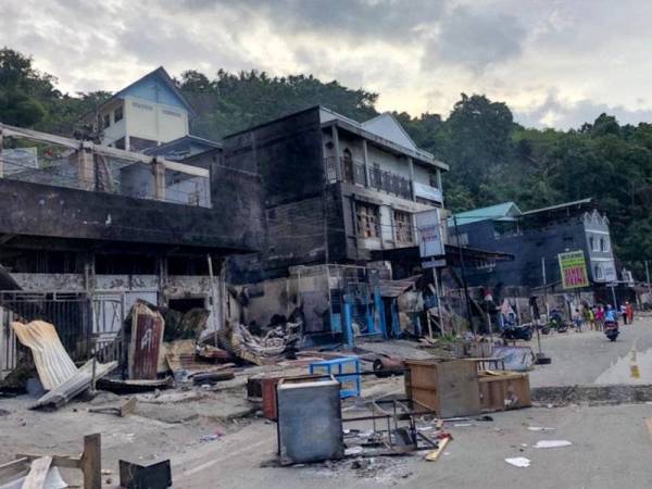 Penduduk berdiri di luar bangunan kedai yang dibakar di Jayapura pada 30 Ogos lalu susulan protes besar-besaran baru-baru ini di Papua. - Foto AFP