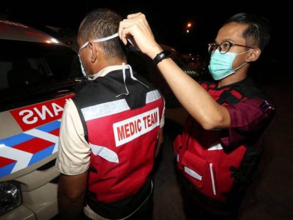 Kakitangan Hospital Jasin Rais Hasif, 27, (kanan) memakaikan penutup hidung dan mulut kepada rakan sekerjanya Zabidi Abd Malek, 45, ketika tinjauan di kilang memproses ayam malam tadi. Foto: Bernama