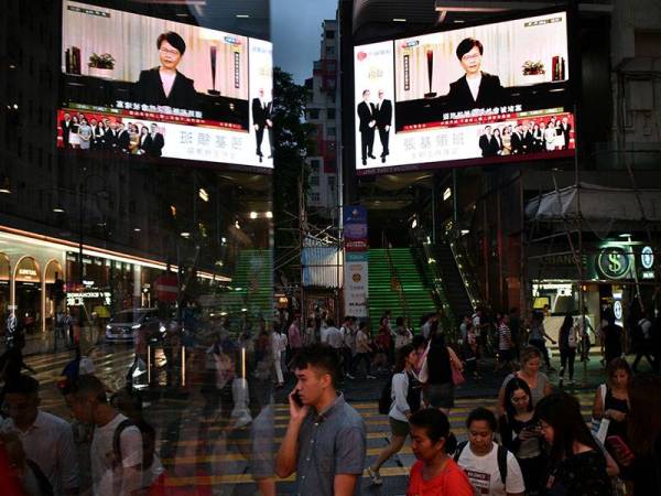 Pejalan kaki berjalan melepasi skrin memaparkan pengumuman penarikan balik rang undang-undang ekstradisi oleh Ketua Eksekutif Hong Kong, Carrie Lam hari ini. - Foto AFP