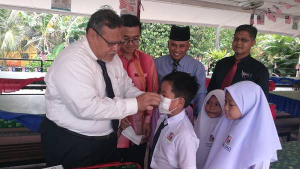 Aminolhuda membantu murid SK Parit Selangor memakai penutup mulut dan hidung ketika mengadakan lawatan ke sekolah berkenaan, tengah hari tadi.