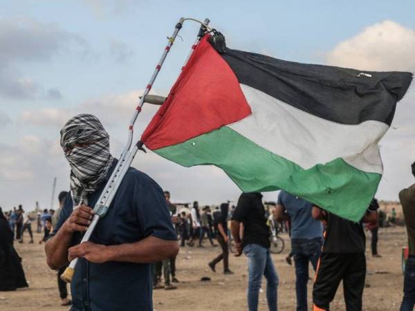 Seorang penunjuk perasaan memegang bendera Palestin ketika pertempuran dengan tentera Israel di sepanjang sempadan Khan Yunis. - Foto AFP