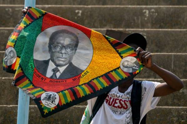 Seorang penyokong bebas Mugabe mengibarkan kain yang memaparkan wajah pemimpin itu ketika berarak di stadium Harare semalam. - Foto AFP