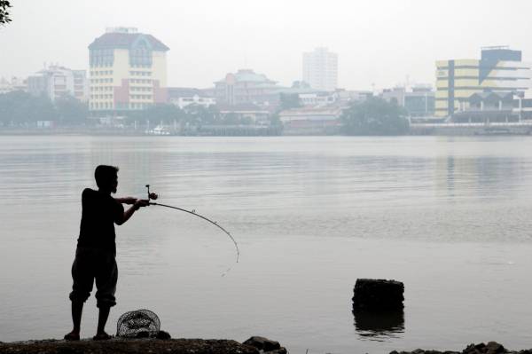 Seorang lelaki kelihatan memancing di Sungai Kuantan dalam suasana jerebu pada tinjauan semalam.
Foto: BERNAMA