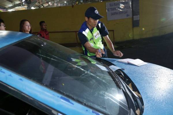 Anggota penguatkuasa MPHTJ meletakkan kompaun di kenderaan wanita terbabit ketika operasi bersepadu di Pasar Borong MPHTJ Batu Berendam di sini hari ini.