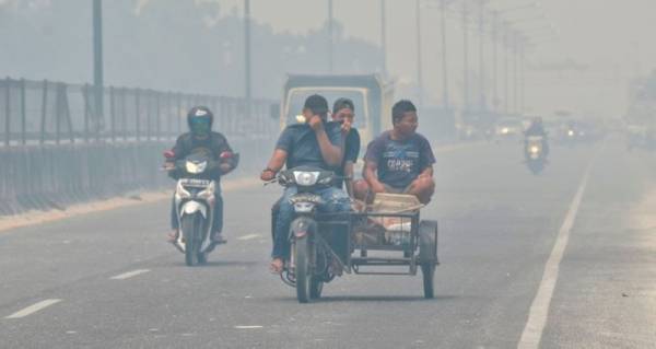 Penunggang motosikal terpaksa menutup hidung ketika melalui sebuah jalan di Kampar, Riau. - FOTO: AFP