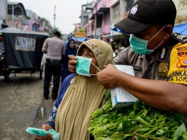 Anggota polis membantu seorang wanita memakai topeng di Banda Aceh semalam. - Foto AFP