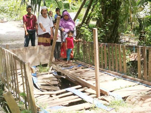 Ramli (depan dari kiri) dan penduduk menunjukkan titi reput yang terpaksa digunakan mereka setiap hari.