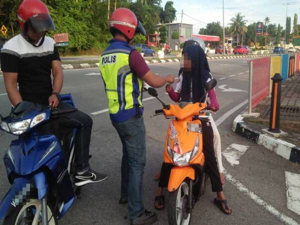 Anggota polis mengeluarkan saman kepada salah seorang penunggang motosikal yang tidak memakai topi keledar di jalan utama depan Pejabat Agama Marang, dalam operasi itu. FOTO: IHSAN IPD MARANG